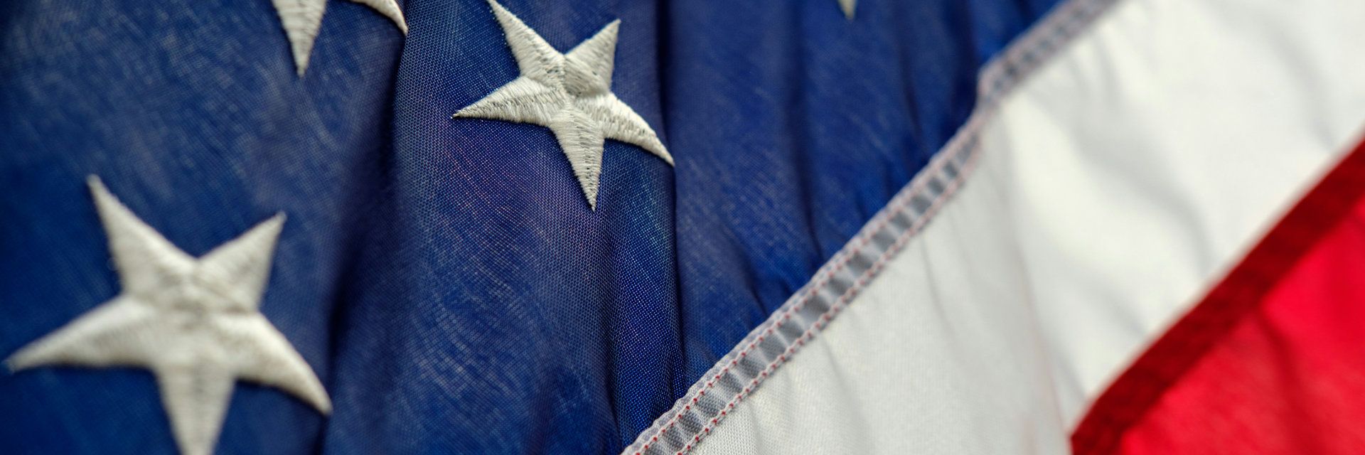 a close up of an american flag showing a few stars on blue, a white stripe and part of a red stripe
